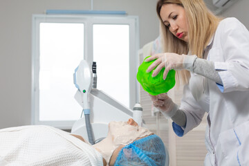 The cosmetologist applying an alginate mask to the face of a young lying woman in beauty salon for procedure of cleansing and moisturizing the skin, removing puffiness and lifting effect