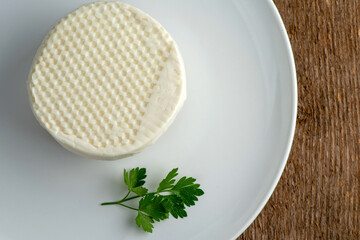 A head of brined cheese, feta, with a sprig of parsley on a white plate.