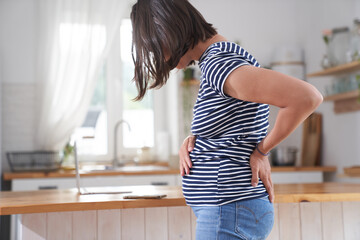 A young pregnant woman holds her stomach with one hand, her back with the other. A brunette woman in the third trimester of pregnancy. The concept of back pain during pregnancy. High quality photo