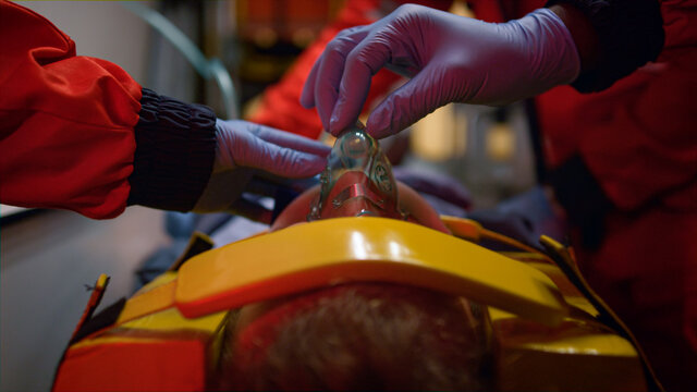 Team of paramedics in gloves giving first aid help to patient in ambulance car