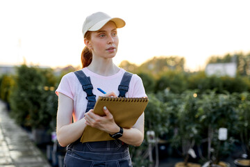 serious woman researcher at work in greenhouse, in working uniform with notepad and pen. Greenhouse...