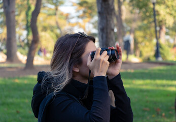 Female photographer, taking pictures with her digital camera of forest landscape at sunset. A girl in black is taking photograph in forest. Green background. Unrecognizable person. 