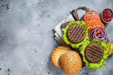 Plant based meatless burgers with vegan grilled pattie, tomato and onion on a wooden serving board. Gray background. Top view. Copy space - obrazy, fototapety, plakaty