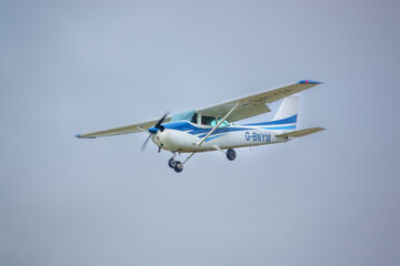 Fototapeta na wymiar G-BNYM Cessna 172N Skyhawk Kestrel Syndicate AAC Middle Wallop (EGVP), UK - high wing trainer light aircraft flying in to land on a grass runway, light cloud sky