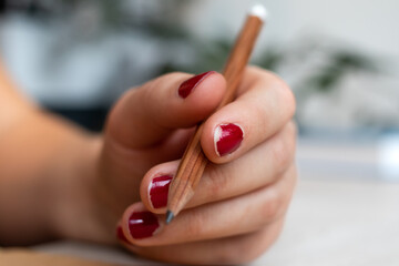 Chipped red nail polish on office woman's hands holding wood pencil