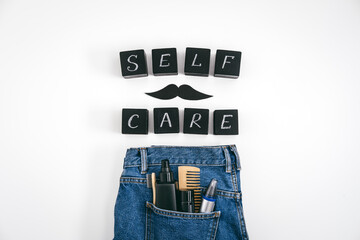 Men self care concept with blue denim jeans and set of male care products and devices and black block with text Self Care on white background.