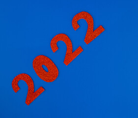 Happy New Year 2022. Christmas background with red glittering numbers 2022 close-up on blue background. View from above. Place for your text.