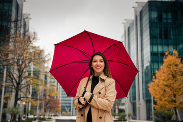 Portrait of smiling woman holding red umbrella on a rainy day.