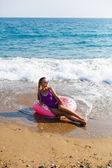 Vacation at the sea. Beautiful slender woman in a swimsuit with an inflatable ring on the beach. Girl resting in the summer on the turkish coast