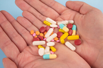 Man holding assorted multicolored medicine pills, capsules and tablets in his hands. A handful of pills. Immune system vitamins and supplemets. Dietary bio supplements