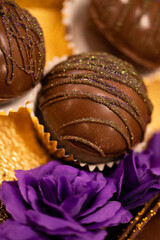 close up of sweet chocolate balls in paper wrapping resting on golden foil paper