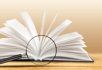 Magnifying glass and open books with turning pages on the table. Reading and studying concept.