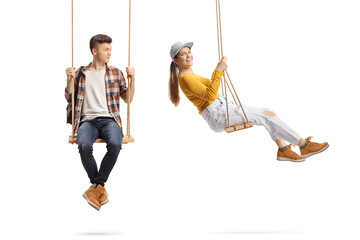 Male teen sitting on a swing and looking at a young female swinging