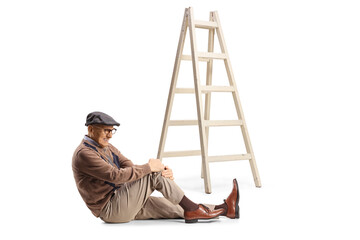 Elderly man sitting on the floor next to a ladder holding his hurt knee