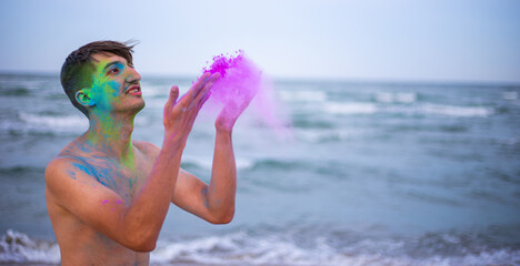 A young guy throws colour powder against the background of the sea