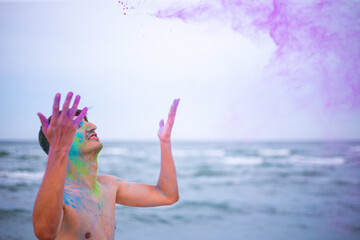 A young guy throws colour powder against the background of the sea