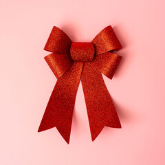 Red sparkly bow laid on pink background. Christmas gift and greeting card idea. Minimal flat lay concept.
