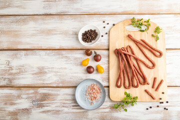 Polish smoked pork sausage kabanos on cutting board with salt and pepper on white wooden background. Top view, copy space.