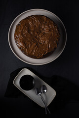 Overhead view of a whole chocolate frosting cake over an elegant dark background.