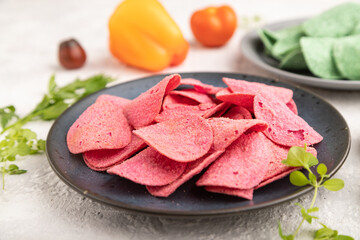 Green and red potato chips on gray concrete background. Side view, close up, selective focus.