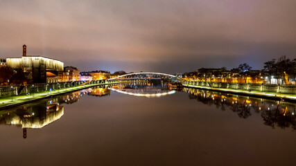 Wieczorne ujecie rzeki Wisła w centrum Krakowa z oświetlonymi budynkami po jej brzegach - obrazy, fototapety, plakaty