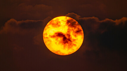 Zbliżenie słońca w czasie zachodu, częściowo przesłonięte chmurami