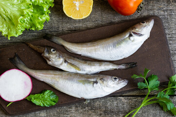 Fresh uncooked haddock fishes on rustic background, raw whiting fish concept