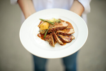 hands holding a plate of cooked meat