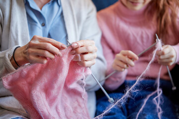 Fototapeta premium Close-up Hands Of Caucasian Grandma And Kid Girl Knitting At Home, Sitting On Sofa, Pretty Little Blond Lady Knitting, Grandmother Is Helping And Teaching. Leisure, Hobby, Weekend, Family Concept