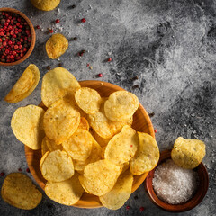 Chips, potato crisps heap with garlic, rosemary, in bowl on grey stone background. Junk food or fast food.