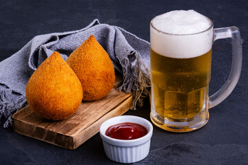 Traditional fried coxinha stuffed with chicken and a mug of cold beer