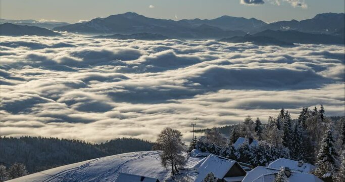 Time lapse of inversion clouds moving in alpine valley. Beautiful landscape in winter season. Small village in the mountains in Slovenia. Low moving fog with long shadows. Aerial or elevated view