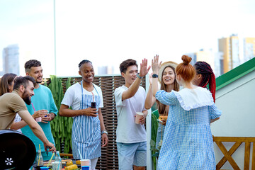 Group of young Happy friends greeting redhead woman friend came at barbecue party. Side View portrait of excited african chinese caucasian students friends in casual wear gathered in terrace