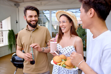 Group Of Young Diverse Friends People Eating Burgers Sandwich On Backyard Terrace Of House, Gathered Together At Summer Evening, Spending Weekends With Friends. Unity, Youth, Friendship Concept