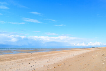 The long sandy beach by the Channel Sea in Europe, France, Normandy, Ouistreham, in summer on a sunny day. - obrazy, fototapety, plakaty