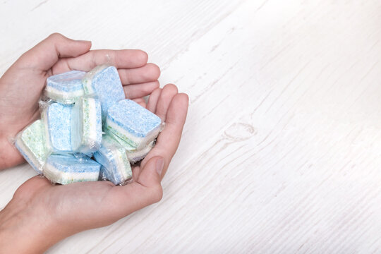 Hands holding many green and blue dishwasher soap tablets in water-soluble packaging, copy space