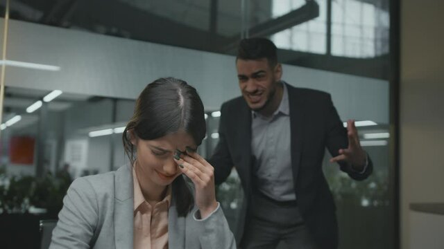Gender discrimination at office. Portrait of young desperate woman employee crying, her angry colleague shouting at her