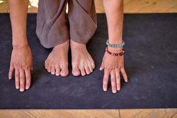 Close-up hands of young woman doing yoga or pilates exercises, training on fitness mat. unrecognizable sportive woman performing forward bend practising yoga uttanasana asana pose. wellness concept