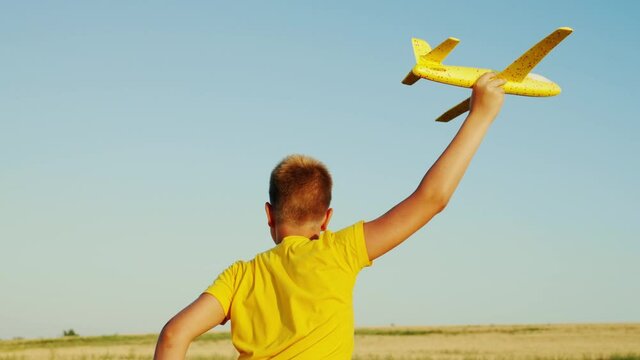 The boy dreams of flying. Happy child running in the park, playing with a toy airplane in summer. Child, boy runs with a toy plane in the field. Carefree child playing outdoors. Happy family