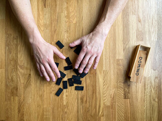 Male hands stir dominoes on a wooden table, top view