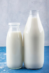 Pure milk drinks in clear jars and bottles are naturally healthy foods placed  on a blue background. A bottle of milk and glass of milk on a wooden table on a blue background.