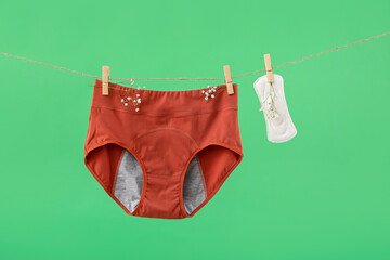 Period panties, pad and gypsophila flowers hanging on rope against green background
