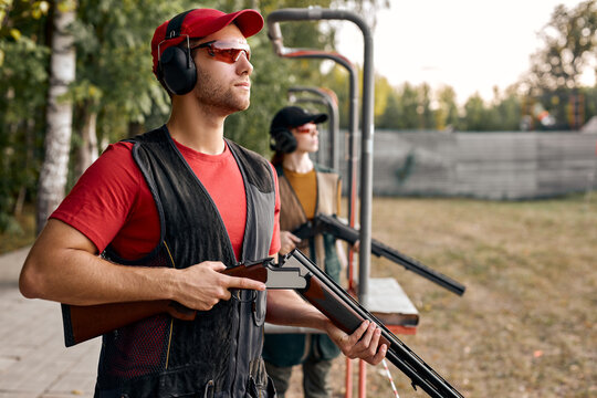 Side View On Male And Female In Outdoor Range, Looking At Side At Target, After Shooting, Concentrated on Training, At Summer Season, Wearing Protective Equipment Uniform, Goggles And Headset