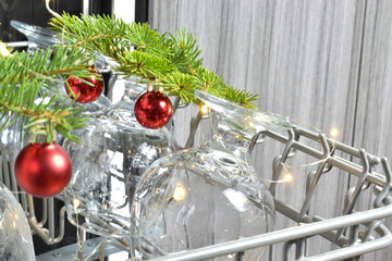 Glass glasses in the dishwasher compartment with Christmas branches and glass red balls.