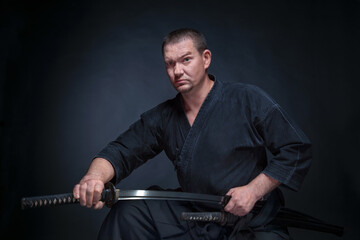 A man in a samurai kimono holding a katana in his hands on a black background, studio session