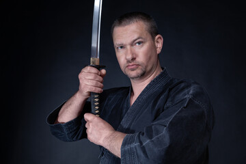 Close up of young martial arts fighter with katana in his hands on a black background