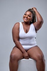 Plump young woman in white bodysuit posing at camera, on white background. Beautiful plus size...