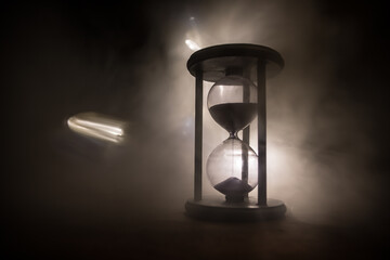 Time concept. Silhouette of Hourglass clock and old vintage wood clock with arrow and smoke on dark background with hot yellow orange red blue cold back lighting, or symbols of time with copy space