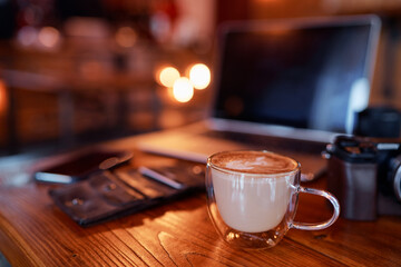 Traveler's breakfast. Cup of cappuccino on wooden table with laptop and photocamera.