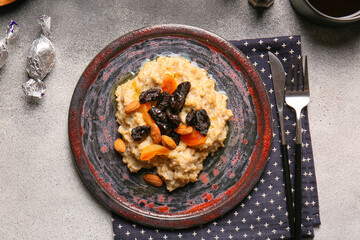 Tasty oatmeal with prunes, dried apricots and almond nuts in plate and cutlery on grey and white background